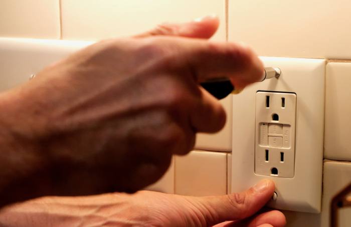 Close-up photo of a hand unscrewing a screw on an electrical outlet plate